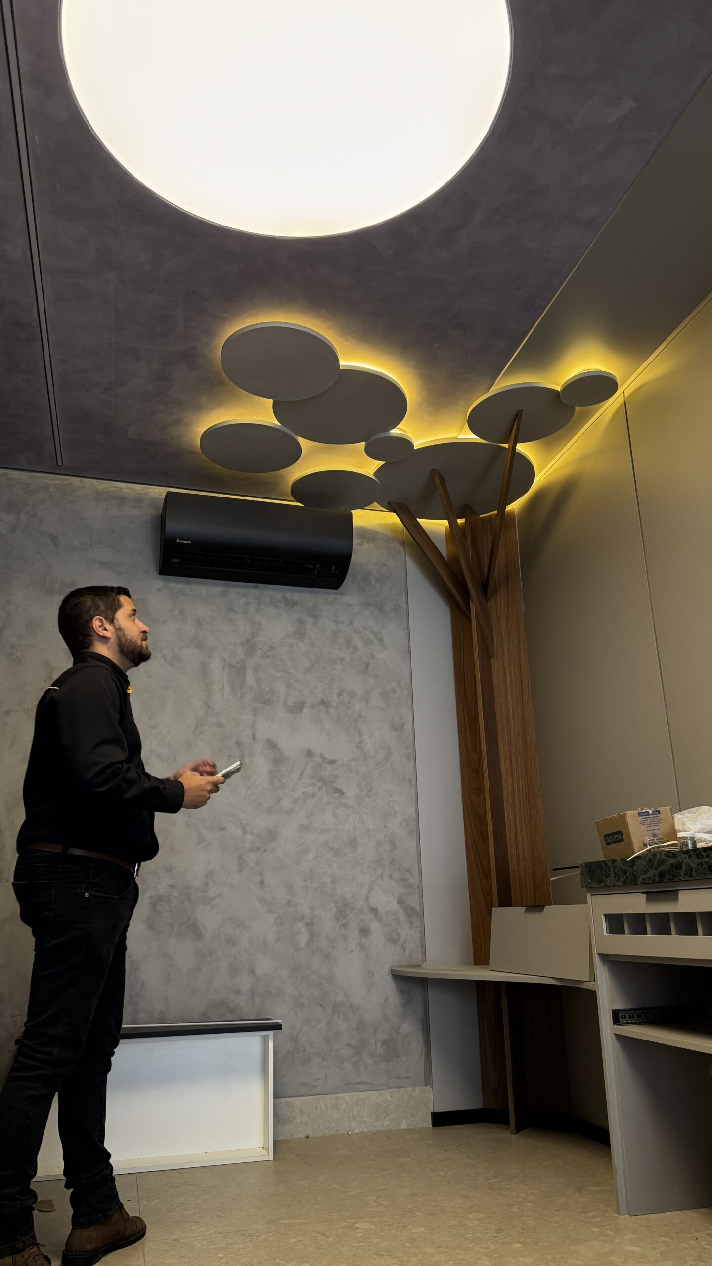 Profissional com celular em ambiente com iluminação no teto e ar-condicionado.